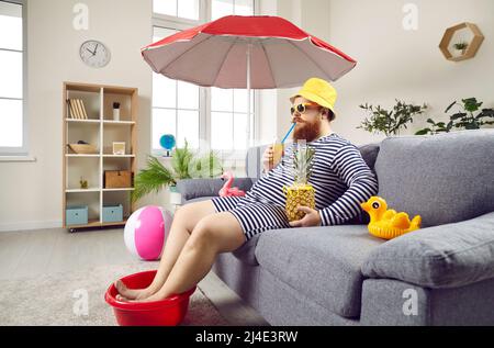 Drôle d'homme dans la salle de séjour à la maison imagine qu'il se repose sur la mer et de bains de soleil sur la plage. Banque D'Images