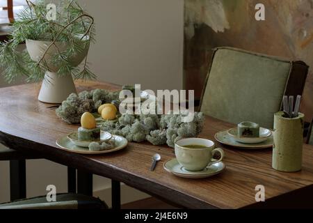 Table pour le dîner de Pâques décorée de mousse forestière, œufs colorés avec du thé matcha dans un plateau de ciment vert mousse. Table en chêne massif contre du texte en argile Banque D'Images