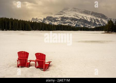 Les chaises rouges emblématiques dans la neige en face du lac Two Jack dans le parc national Banff, Alberta, Canada Banque D'Images