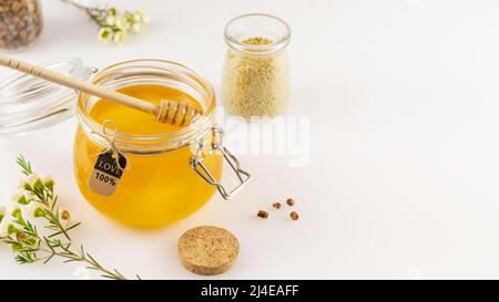 Composition de soins de santé avec miel organique et propolis en pots de verre avec un balancier de miel sur une table blanche avec fleurs et espace de copie. Les produits de l'abeille sont Banque D'Images