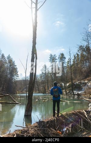 Photographe avec un sac à dos sur ses épaules et avec un appareil photo reflex numérique dans son et marche le long du barrage du castor et recherche une photo Banque D'Images