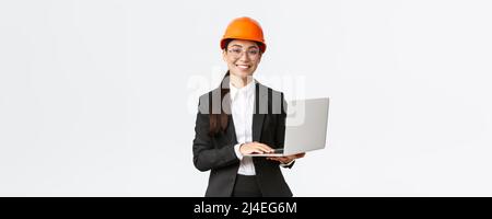 Femme de vente souriante professionnelle montrant des travaux de construction sur une nouvelle maison. Ingénieur industriel asiatique en casque de sécurité et combinaison de travail utilisant Banque D'Images