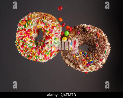 Deux beignets sucrés multicolores avec glaçage au sucre et asperges de confiserie. Isolé sur un fond gris. Bonbons, nourriture pour enfants, culture jeunesse, foo rapide Banque D'Images