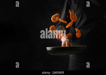 Un chef professionnel en uniforme noir cuisine des crevettes tigrées sur fond noir. La lévitation. Recettes de fruits de mer. Plats gastronomiques. Restaurant, hôtel, Banque D'Images