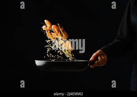 Crevettes tigrées dans une casserole dans un vol gelé sur fond noir dans la main du chef. Cuisine de fruits de mer, cuisine asiatique, plats gastronomiques. Végétarien sain Banque D'Images