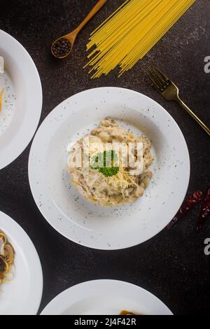 un spaghetti de pâtes cuit carbonara avec sauce à la crème, tranche de boeuf, huile d'olive et persil vert frais dans une assiette ovale blanche avec des ingrédients sur le tableau noir Banque D'Images