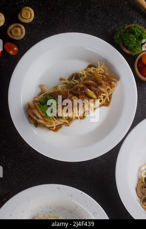 un spaghetti cuit aux pâtes avec sauce au poivre noir, une tranche de bœuf, de l'huile d'olive et du persil vert frais dans une assiette ovale blanche avec ingrédients Banque D'Images