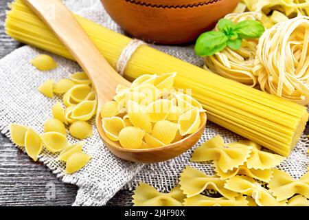 Pâtes de coquillages dans une cuillère, tuyau de rigate dans un bol, spaghetti, tagliatelle, farfalle, trenette sur toile de fond en bois Banque D'Images