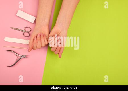 Mains avec une manucure de couleur naturelle à côté des instruments pour la procédure sur fond vert Banque D'Images