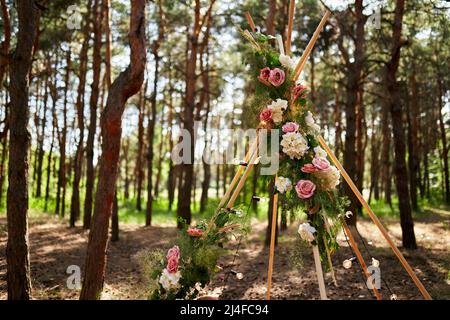 Arche de tipi de Bohème en tiges de bois décorées de roses roses roses, bougies sur la moquette, herbe de pampass, enveloppée de lumières de fées sur le mariage extérieur Banque D'Images