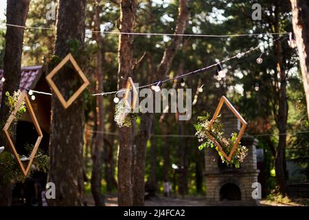 Réception de mariage à l'extérieur dans la forêt de pins. Tables à manger, bancs décorés dans le style boho avec bougies, fleurs, lumières de fée printanière, assiettes Banque D'Images