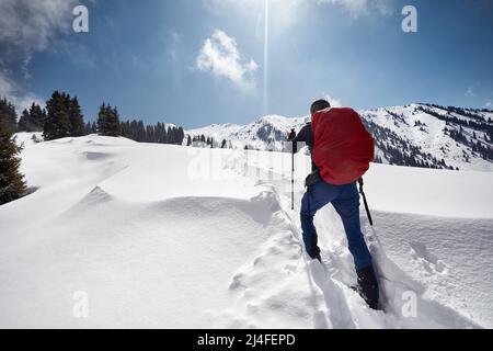 Homme avec sac à dos marchant sur la colline de neige dans les belles montagnes contre le ciel bleu à Almaty, Kazakhstan Banque D'Images