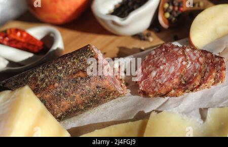 Salami au poivre sur plateau avec fromage anglais et irlandais, pommes en tranches et épices dans une cuisine rustique avec fenêtre de la cuisine Banque D'Images