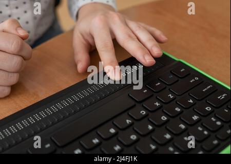 Une femme aveugle utilise un ordinateur avec un écran en braille et un clavier d'ordinateur. Périphérique inclus. Banque D'Images