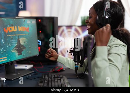 Heureux gagnant de cyber-femme assis au bureau de jeu jouant à esport jeux vidéo gagnant en ligne championnat. Un joueur professionnel qui a réussi à diffuser en direct en utilisant un équipement informatique RVB. Loisirs Banque D'Images