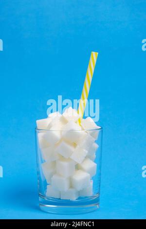 Verre avec cubes de sucre raffiné et un tube à boire sur fond bleu Banque D'Images
