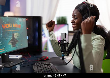 Une joueuse professionnelle heureuse et excitée se levant les mains après avoir remporté un jeu de tir spatial. Le gagnant qui a réussi à jouer à des jeux vidéo en ligne en utilisant l'équipement informatique RBG. En studio à domicile. Espace cybernétique Banque D'Images