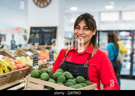 Femme latine travaillant dans un supermarché tenant une boîte contenant des avocats frais Banque D'Images