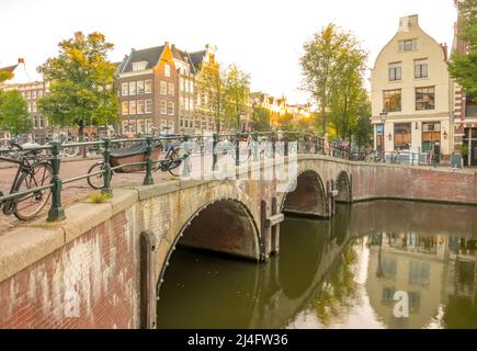 Pays-Bas. Pont en pierre avec trois arches sur le canal d'Amsterdam. Beaucoup de vélos garés. Les premiers rayons du soleil le matin Banque D'Images