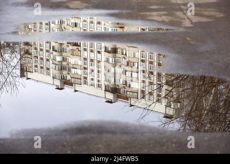 Flaques après la pluie avec réflexion de bâtiment résidentiel dans l'eau. Rue de la ville par temps pluvieux au printemps Banque D'Images