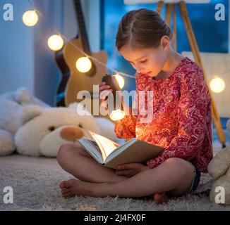 Adorable petite fille lisant le livre la nuit Banque D'Images