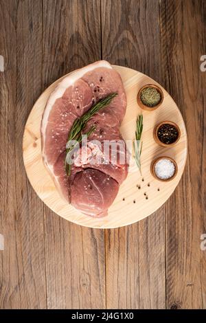 la chair du porc sur l'os repose sur une planche à découper et une table en bois avec une branche de romarin . Vue verticale du dessus Banque D'Images