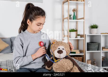 fille jouant docteur avec ours en peluche et jouet stéthoscope dans la chambre Banque D'Images
