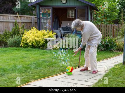 Grand-mère s'amusant avec des bulles dans le jardin prouvant que vous n'êtes jamais trop vieux pour être un enfant! Concept de jeune à coeur. Banque D'Images