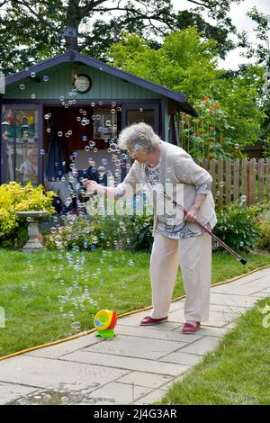 Grand-mère s'amusant avec des bulles dans le jardin prouvant que vous n'êtes jamais trop vieux pour être un enfant! Concept de jeune à coeur. Banque D'Images