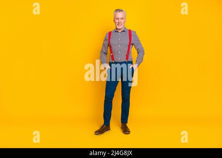 Vue sur toute la longueur du corps d'un homme d'âge moyen agréable et gai tenant les mains dans des poches isolées sur fond jaune vif Banque D'Images