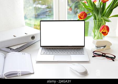 Espace de travail de bureau blanc près de la fenêtre, ordinateur portable avec écran vierge, bouquet de tulipes et fournitures sur un bureau à la maison, maquette, espace de copie, mise au point sélectionnée, nar Banque D'Images