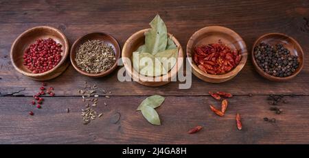 Une rangée d'épices dans de petits bols sur une planche en bois rustique sombre, cuisine et concept alimentaire, format panoramique, vue de dessus de haut en angle Banque D'Images