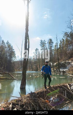 Photographe avec un sac à dos sur ses épaules et avec un appareil photo reflex numérique dans son et marche le long du barrage du castor et recherche une photo Banque D'Images