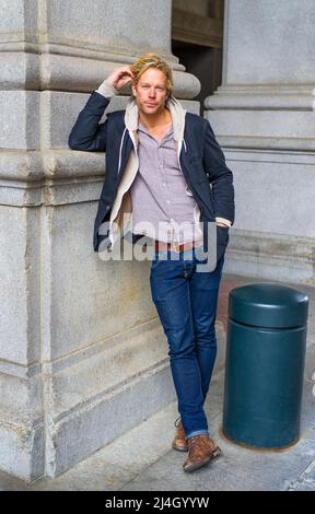 Un jeune homme beau se tient debout à l'extérieur contre une colonne, se grattant la tête et pensant. Banque D'Images