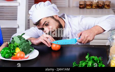 Le chef masculin en uniforme blanc coupe des tomates avec un couteau. Préparation des plats. Régime alimentaire, concept d'alimentation saine Banque D'Images