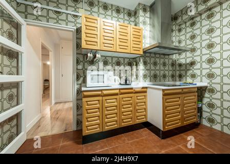 Cuisine avec comptoirs en pierre blanche, armoires en bois massif et carreaux anciens sur les murs, porte en bois avec armoire en verre menant à un couloir blanc an Banque D'Images