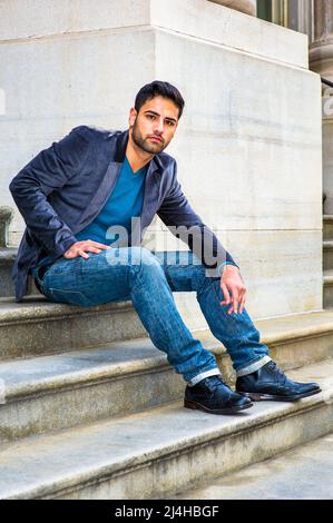 Portant un blazer en laine violet foncé, un Jean bleu et des chaussures en cuir noir, un jeune homme du Moyen-Orient avec du pain et de la moustache est assis sur des marches, Banque D'Images