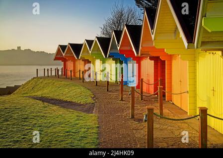 Royaume-Uni, North Yorkshire, Scarborough, Chalets de plage colorés au-dessus de North Bay Promenade avec le soleil levant au-dessus du château de Scarborough Banque D'Images
