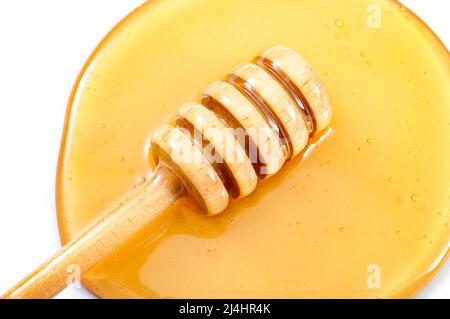 Gros plan sur le miel qui s'égoutte du balancier dans une piscine de miel jaune doux isolée sur blanc Banque D'Images