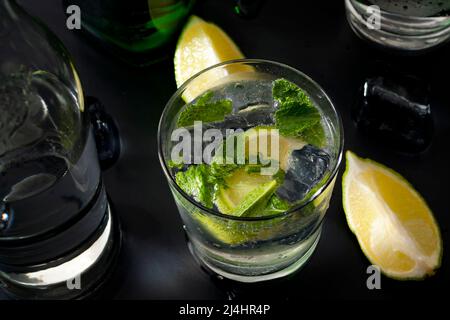 Cocktails rafraîchissants et boissons alcoolisées mélangées avec gros plan d'un verre de gin tonique sur un comptoir de bar avec une bouteille de gin, eau minérale Banque D'Images