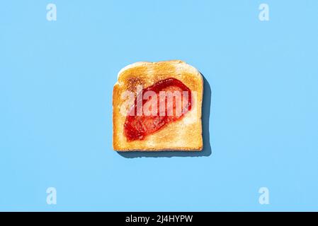 Vue ci-dessus avec une seule tranche de pain grillé et confiture de fraises, minimaliste sur une table bleue. Délicieux confiture de fruits sur pain grillé croquant Banque D'Images