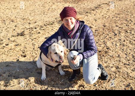 Femme souriante avec un chien sur la plage ensoleillée. Banque D'Images