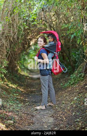 La mère avec un enfant en bas âge dans un sac à dos est en randonnée dans la forêt Banque D'Images