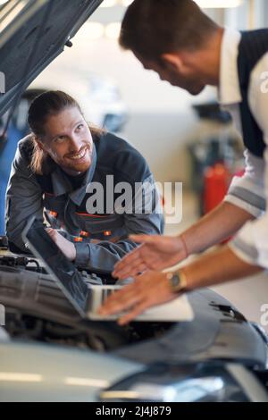 Deux travailleurs dans un atelier automobile effectuant un diagnostic sur une voiture Banque D'Images