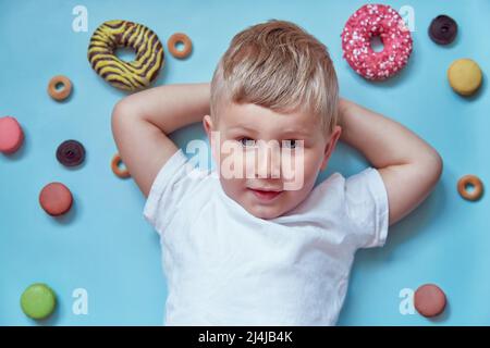 Mignon enfant souriant sur des beignets et des macarons français sur fond bleu. Concept de la Journée nationale du Donut. Concept d'enfance heureuse. T-shirt blanc maquette. Banque D'Images