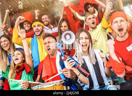 Les fans de football fans applaudissent et regardent le match de la coupe de football au stade de l'intenational - groupe de jeunes avec des t-shirts multicolores Banque D'Images