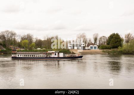 Un bateau de plaisance vide qui passe devant le club nautique Emanuel School Boat Club sur une Tamise placide à Barnes, dans le sud-ouest de Londres, en Angleterre, au Royaume-Uni Banque D'Images