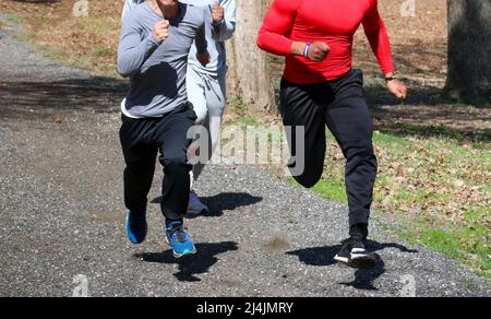 Trois coureurs de piste d'école secondaire qui s'exécutent rapidement sur un sentier en montée dans les bois pour l'entraînement de force pendant la piste et l'entraînement sur le terrain. Banque D'Images