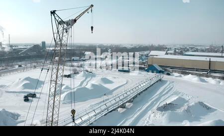 Vue panoramique en hiver. Attache. Une grande grue en production se trouve à côté de la ville et de la route sur laquelle les voitures circulent Banque D'Images