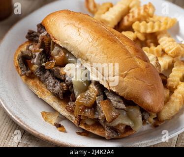 Gros plan d'un sandwich au cheesesteak philly, composé de steak, de fromage et d'oignons, sur un petit pain grillé accompagné de frites sur une assiette Banque D'Images